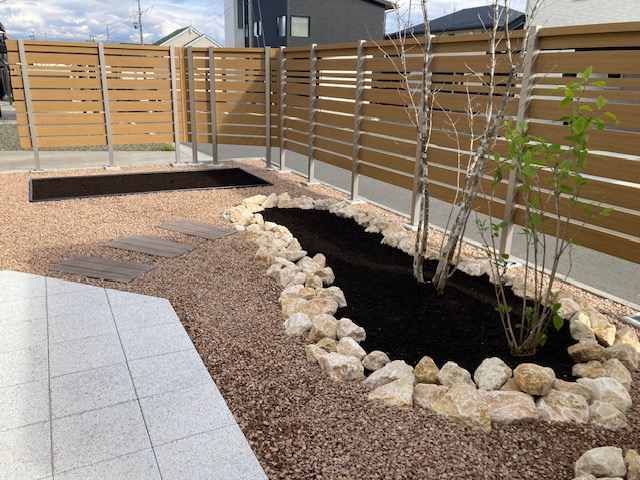 化粧砂利、枕木風平板の園路、景石で縁取りした花壇。草花を植えて、これからが楽しみな花壇です。